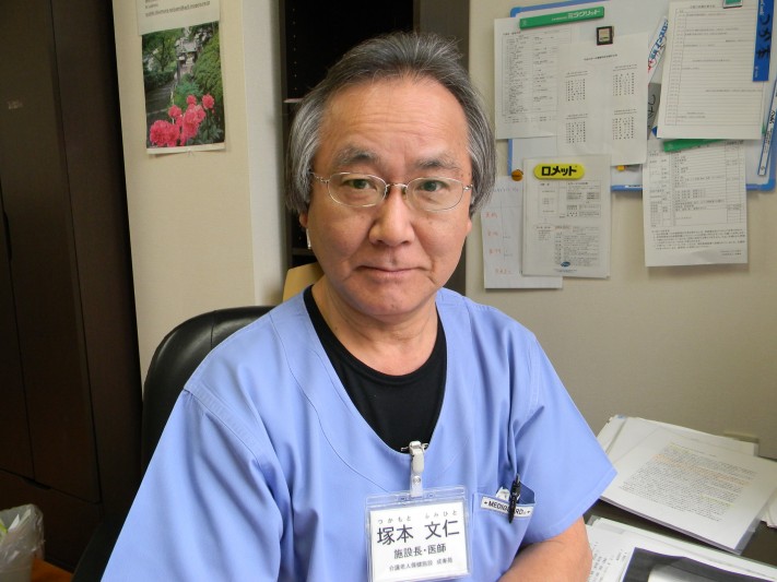 介護施設のスタッフが事務室で撮影された写真。名札を着用している男性職員。